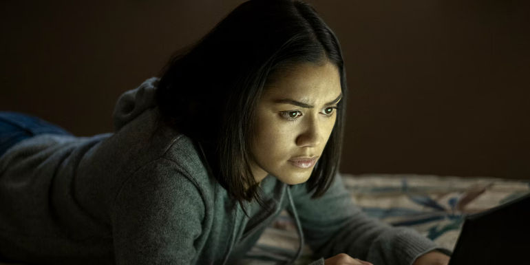 Rose lays on the bed looking at a computer screen in The Night Agent season 1.