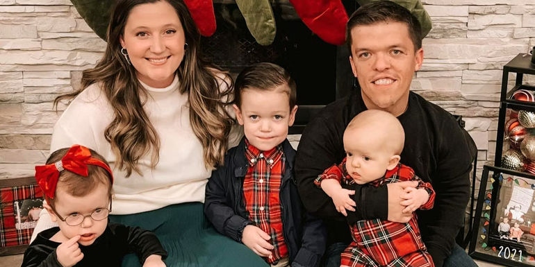 Tori and Zach Roloff with their kids smiling in front of fireplace at Christmastime