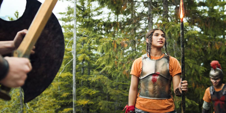 Clarisse looking up at her flaming spear while Percy stands on guard in the Percy Jackson series