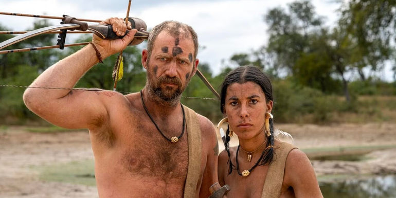 Naked and Afraid season 17 promo of two conestants with mud paint with man holding bow and arrows
