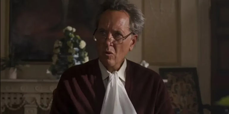 Sir James Catton is sitting at the table, wearing glasses, and has a napkin tucked in his shirt in Saltburn.