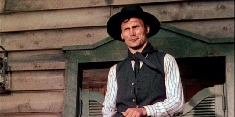 Jack Palance as Jack Wilson gleefully smiling at an off screen foe while reaching for his six shooter in Shane