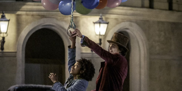 Willy Wonka (Timothée Chalamet) and Noodle (Calah Lane) hold onto a bouquet of balloons in Wonka.