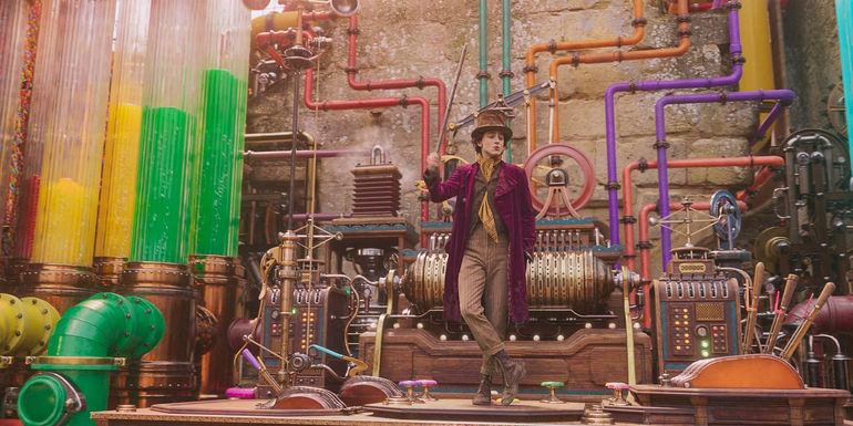 Willy Wonka (Timothée Chalamet) dances in front of colorful pipes and gizmos in his factory in Wonka.