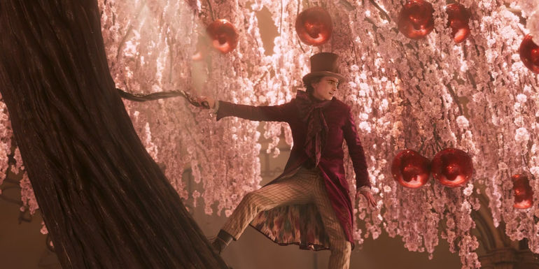 Willy Wonka (Timothée Chalamet) stands on a colorful chocolate tree in Wonka.