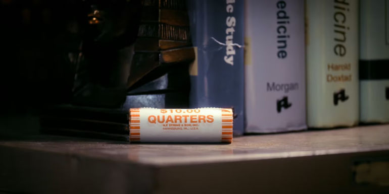 A roll of quarters sits on a shelf in front of textbooks in Community.
