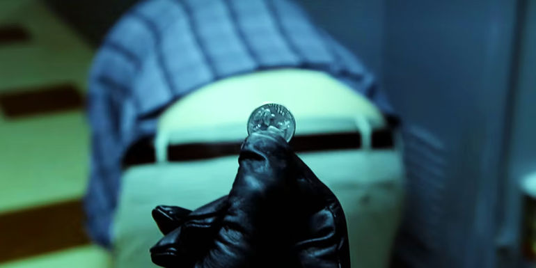 The Ass-Crack Bandit wears black leather gloves while holding up a quarter behind Garrett in Community.