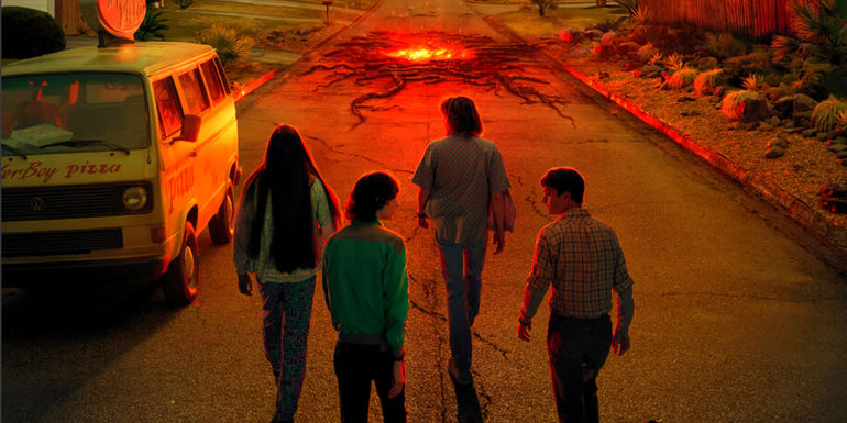 Eduardo Franco as Argyle, Finn Wolfhard as Mike Wheeler, Charlie Heaton as Jonathan Byers, and Noah Schnapp as Will Byers walking down a road with cracks and lava coming up in Stranger Things