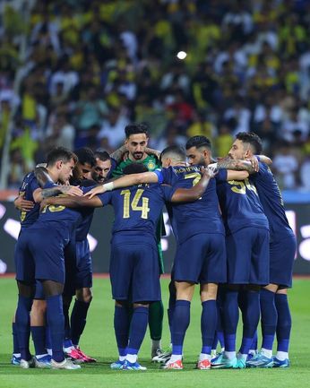 A group of soccer players, including the over-30 Christiano Ronaldo, huddle on a packed stadium pitch, exuding team spirit pre-match.