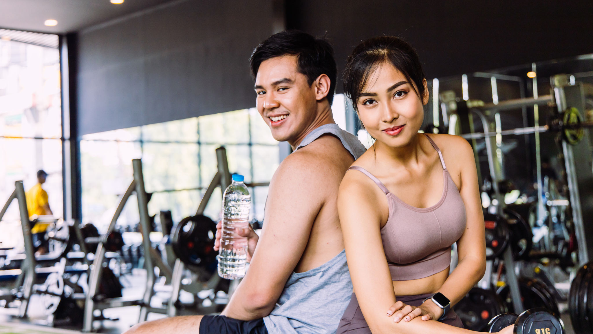 Isang magandang hugis pares ng mga Asyano kalalakihan at kababaihan pakikipag usap sa bench Holding isang bote ng tubig at dumbbells sa isang fitness gym. Mga konsepto ng ehersisyo para sa kalusugan at magandang hugis