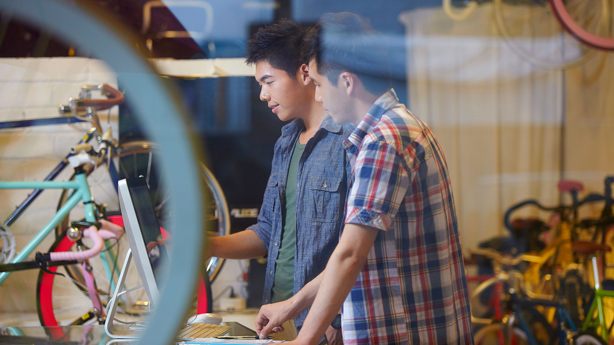 Two young men are looking at something attentively inside a bicycle shop 