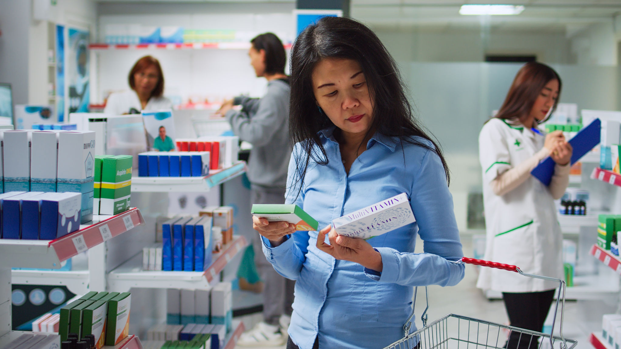 Asian woman examining boxes of medicine on pharmacy shelves  