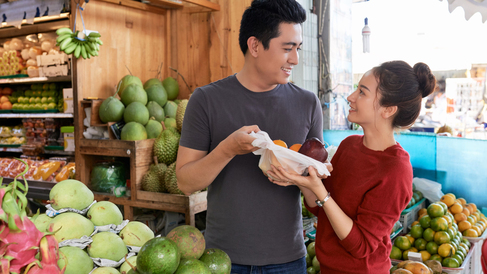 Joyful young Asian couple buying fresh ripe fruits and vegetables