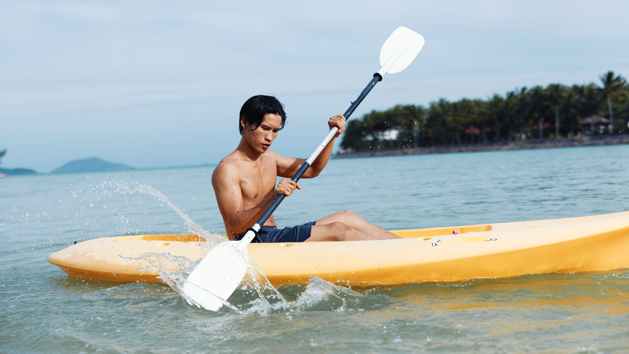 Happy Asian Man Kayaking sa isang Tropical Beach 