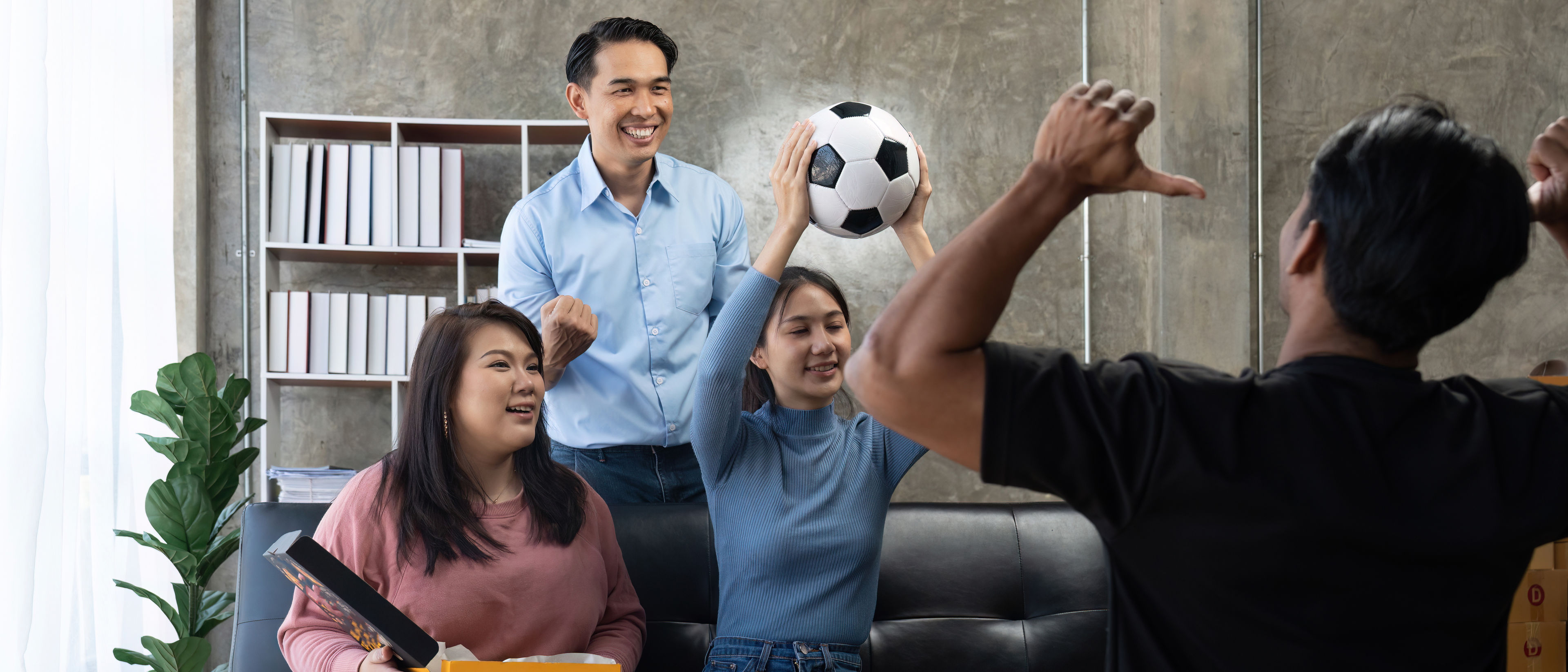 Friends watch sports on TV, cheer and celebrate. Happy diverse Asian friend supporters fans sit on