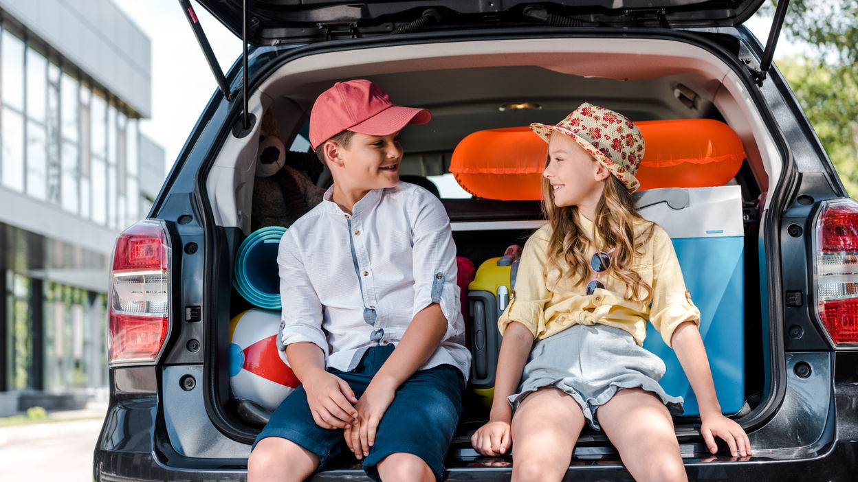 happy-sister-and-brother-sitting-on-car-trunk-and-2023-05-06-00-04-42-utc