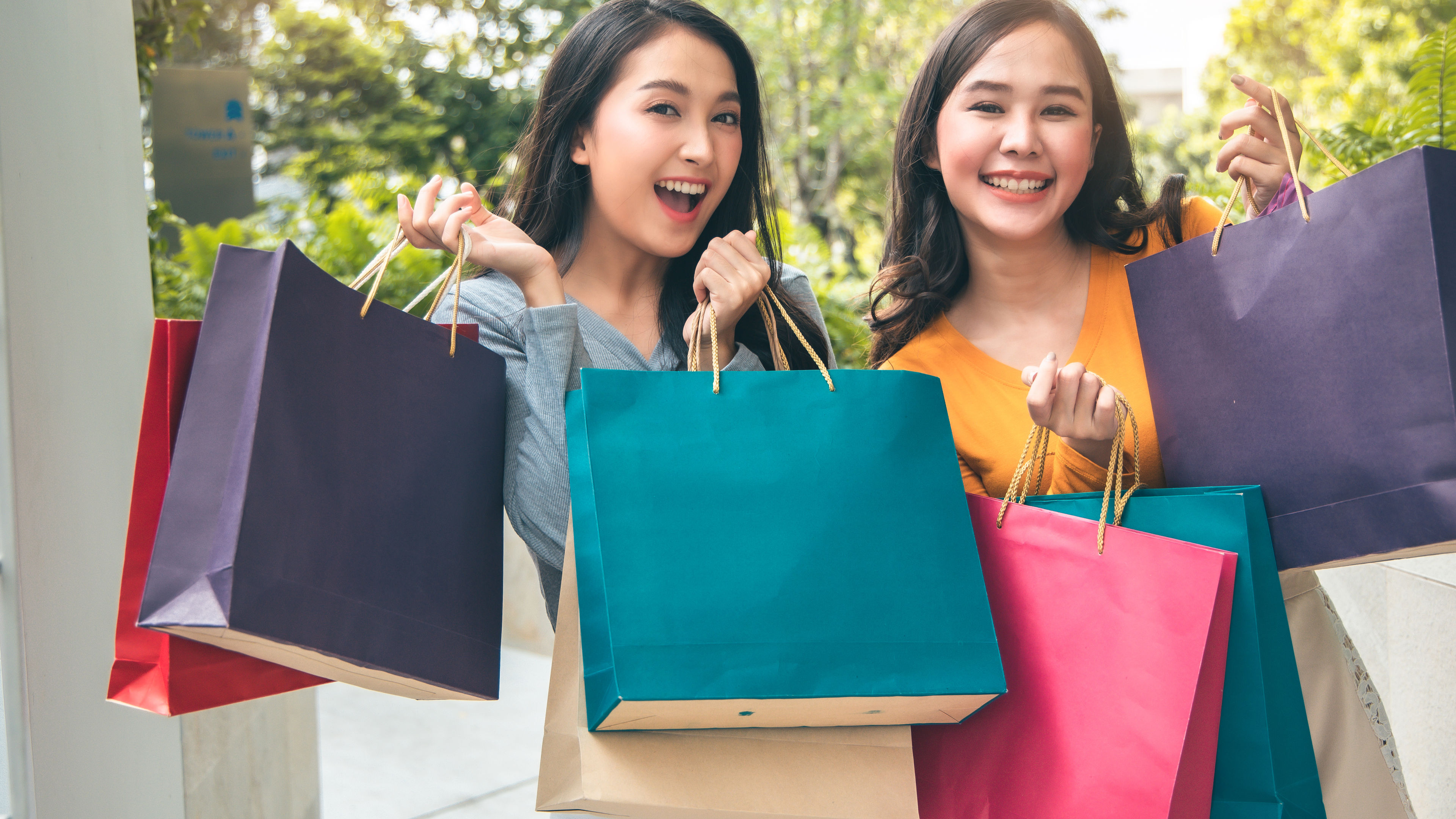 Malaysian female friends nakangiti at nagpo pose na may mga shopping bag sa kamay