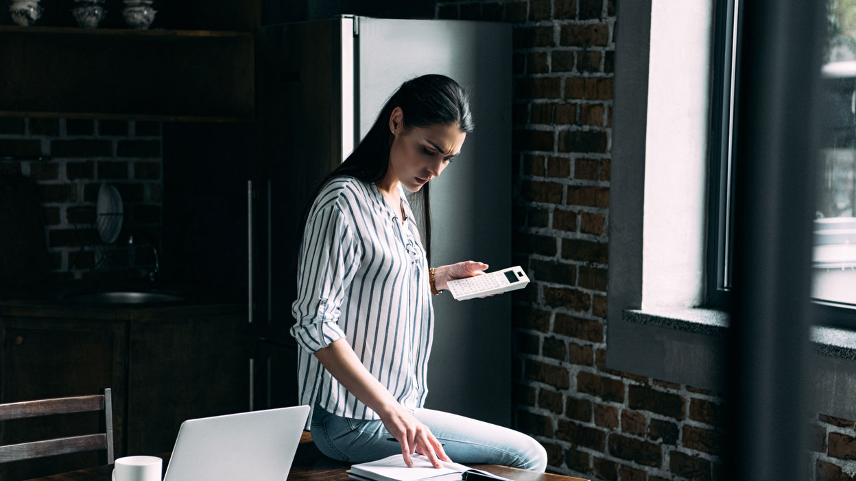 sad-young-woman-with-calculator-counting-tax-on-ki-2022-12-16-20-07-10-utc