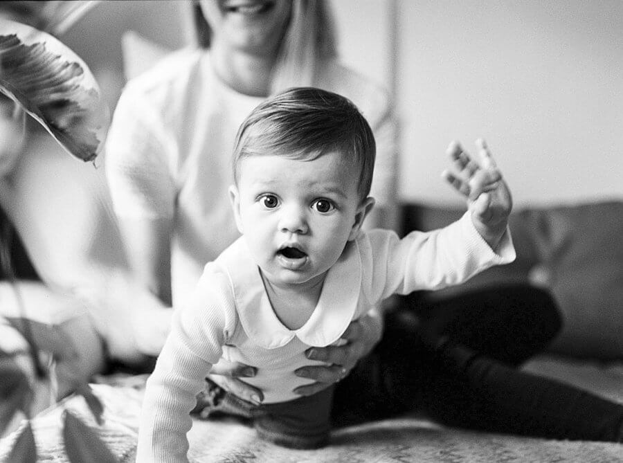 black and white photography of baby looking into camera crawling on sofa