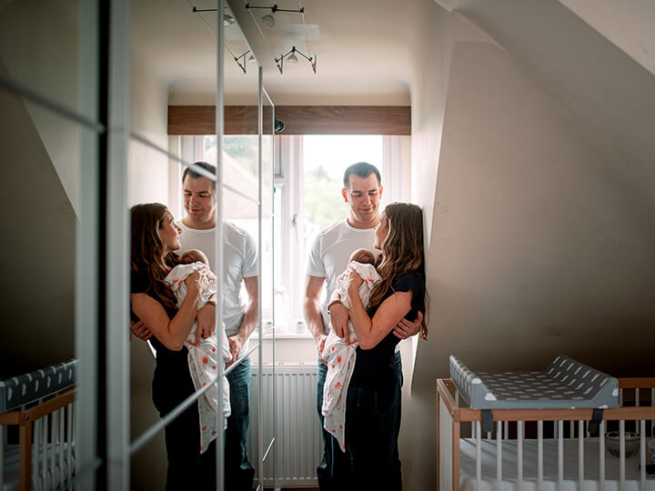 In Home Family Shoot London Parents and Newborn Baby standing together with a mirror reflection.