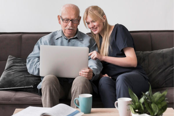 smiley-nurse-showing-old-man-laptop 1 (1)