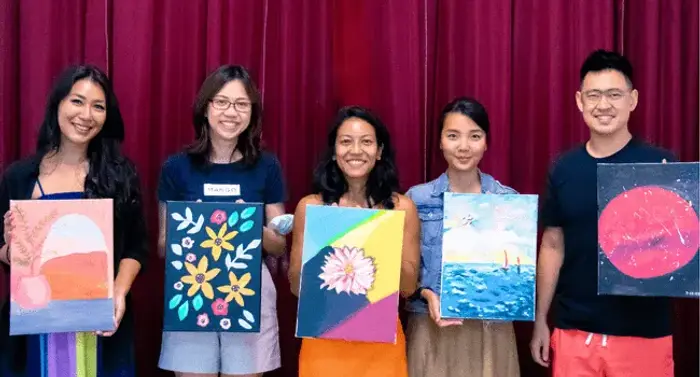 Five colleagues hold up the canvases they each painted
