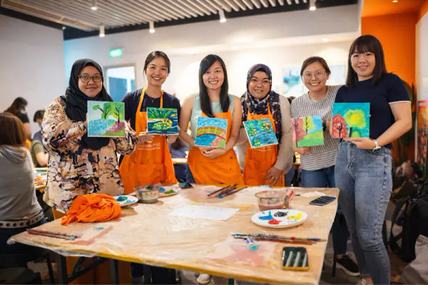 A group gathered behind a table of finished paintings