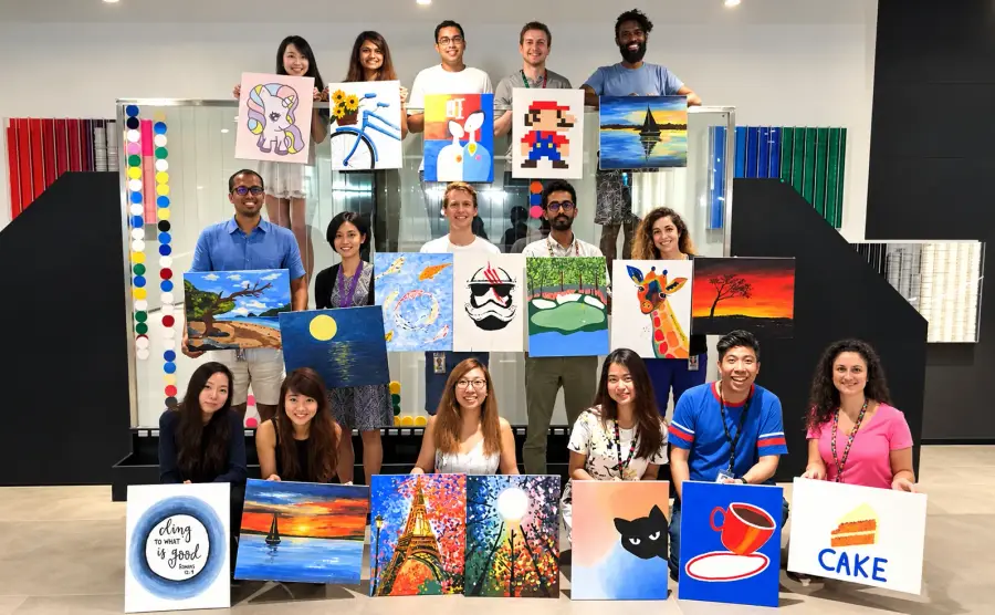 A company group hold up the canvases they each painted