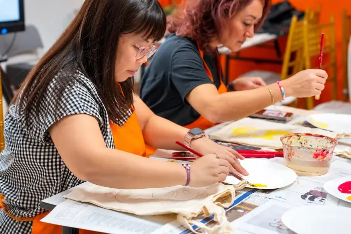 Two participants paint their tote bags at a FunEmpire session