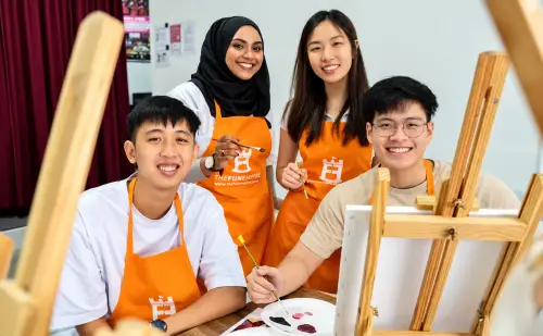 Four friends in FunEmpire aprons smile beside an easel as they paint