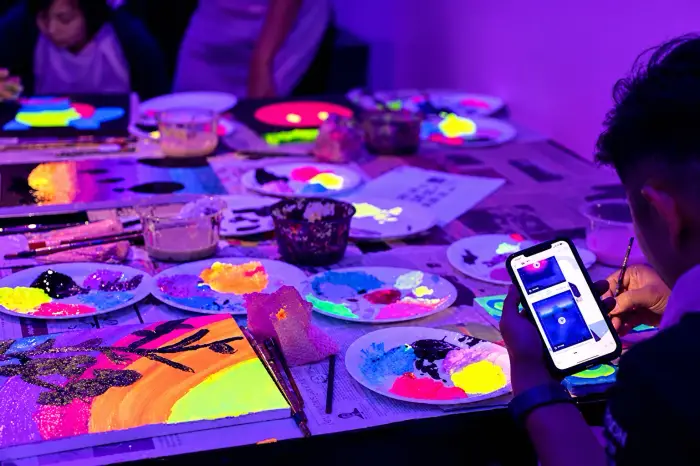 Palettes of neon paint glow under UV light on a worktable