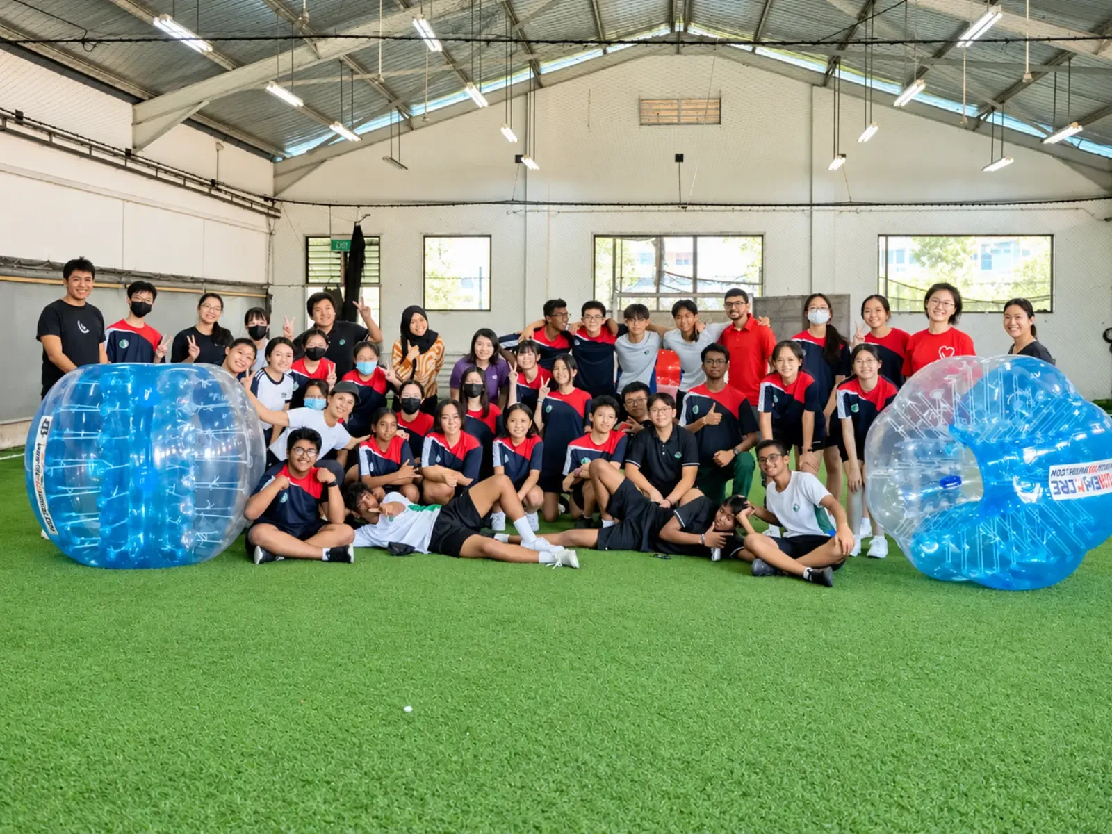 A large school group gathers on the turf with their bubble suits