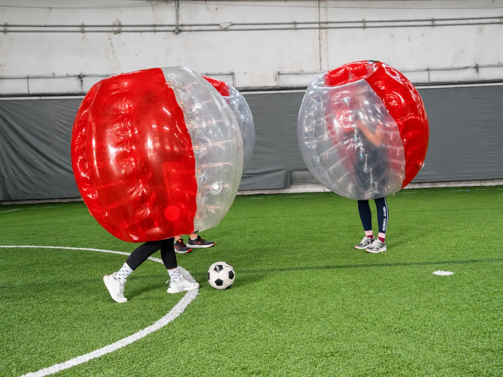 Two players chase the ball in bubble suits on the turf