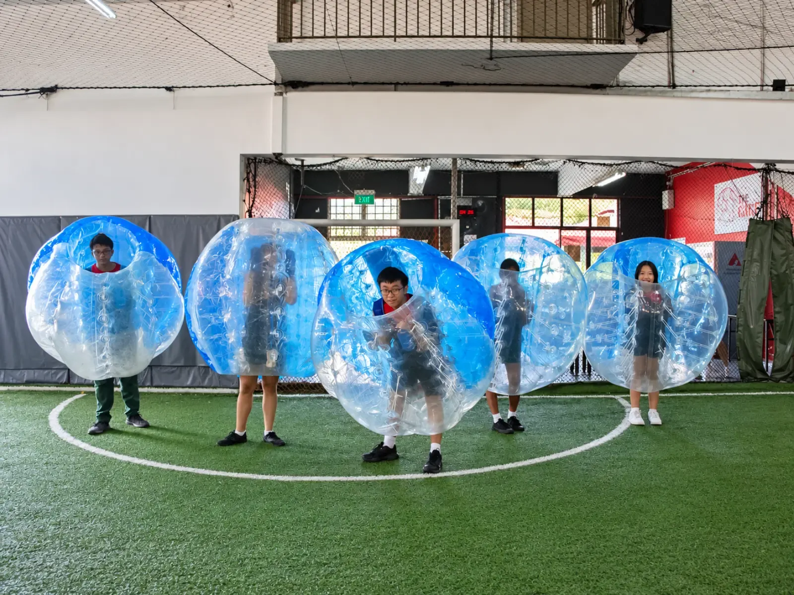 A line of players in bubble suits on a sheltered indoor pitch