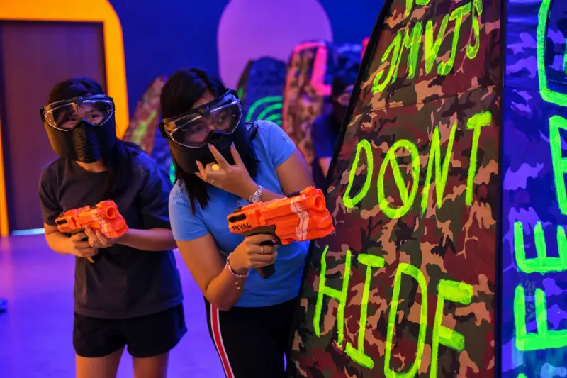 Two players in masks move up beside a bunker, blasters in hand