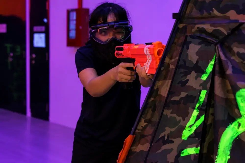 A player in goggles and a mask takes aim past the edge of a bunker