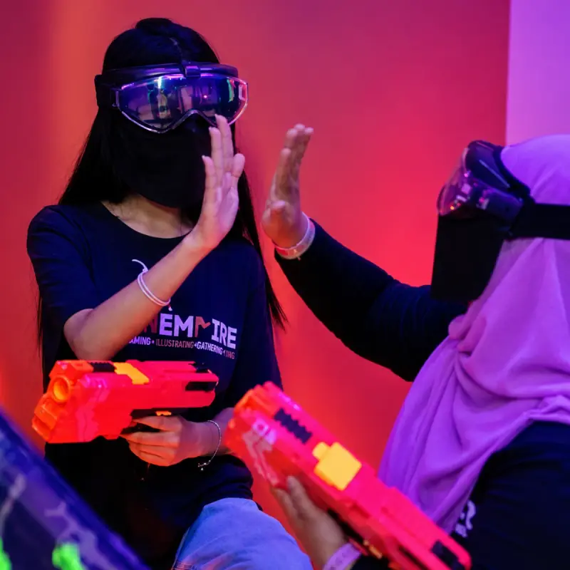 Two players in masks share a high-five, blasters in hand
