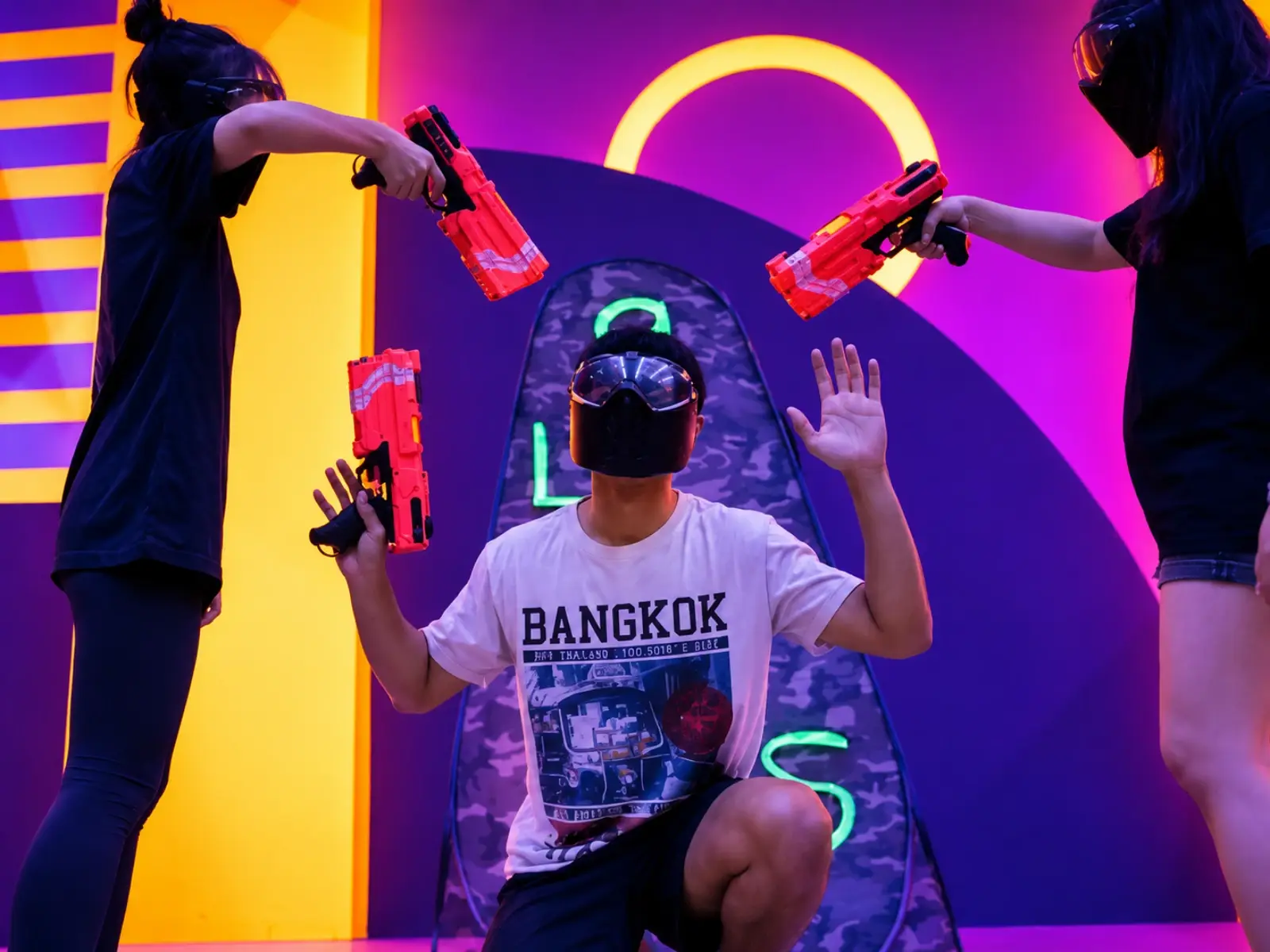 A player kneels with his hands up as two opponents point their blasters at him