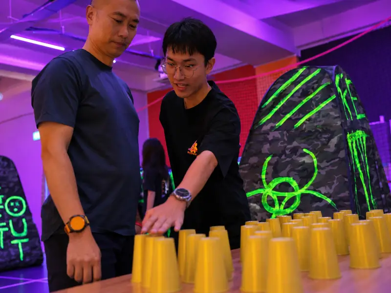 Two players set out a row of yellow cups on a table in the studio