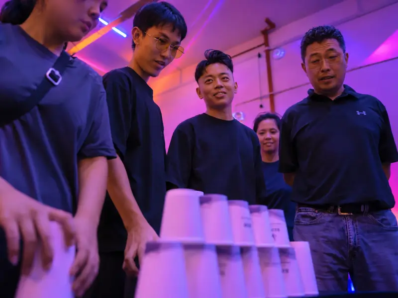 A team gathers round a wall of stacked paper cups