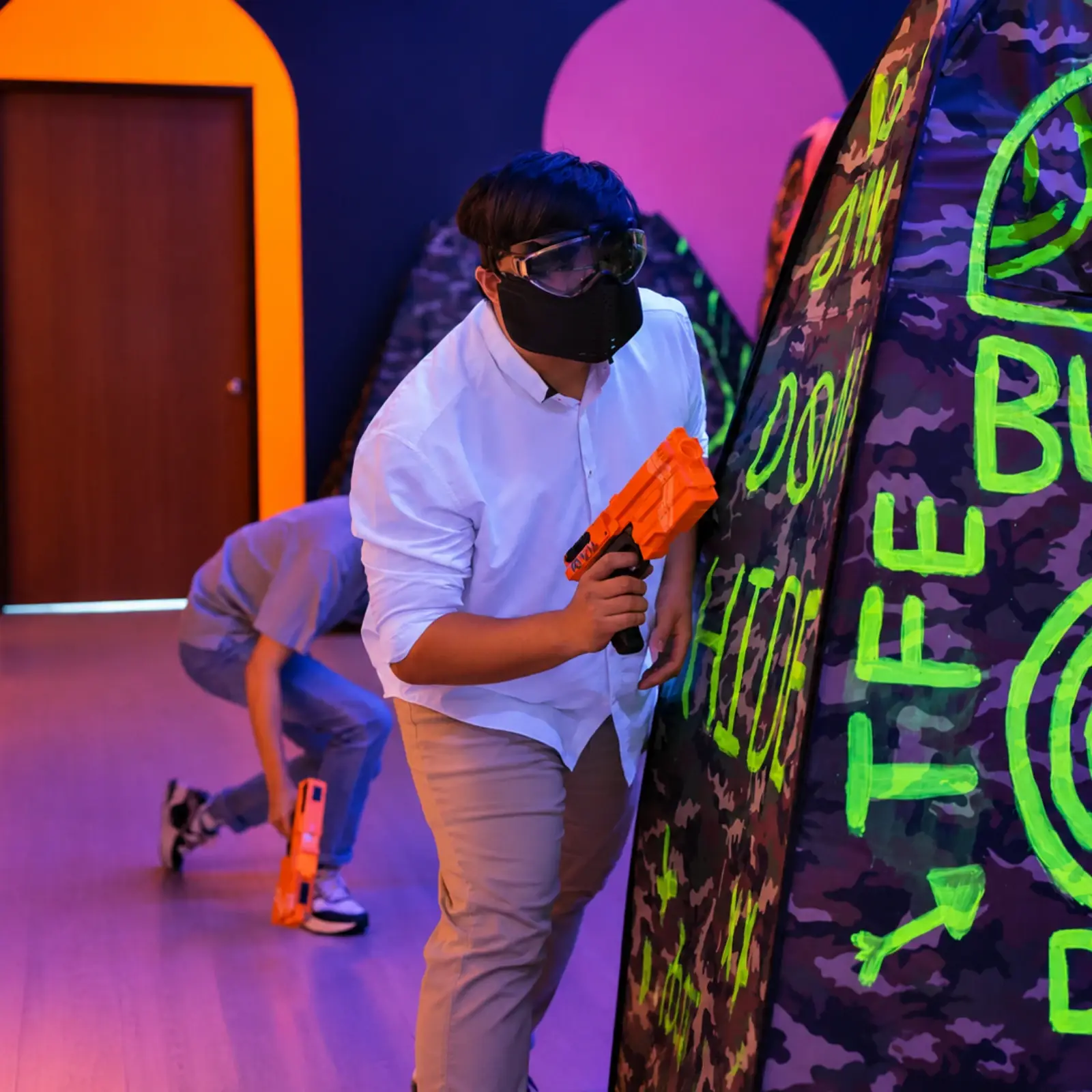 A player presses up against a bunker, blaster ready, while a teammate crouches behind him