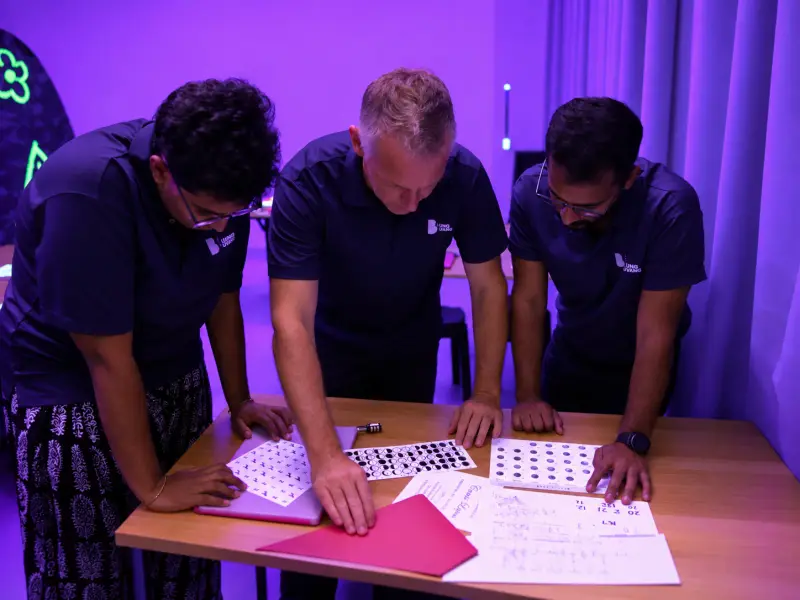 Three teammates bend over the puzzle sheets, heads together