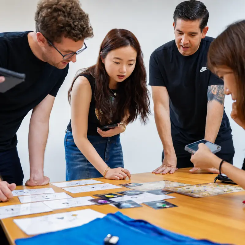 Four colleagues lean over a table of puzzle cards, working out a clue