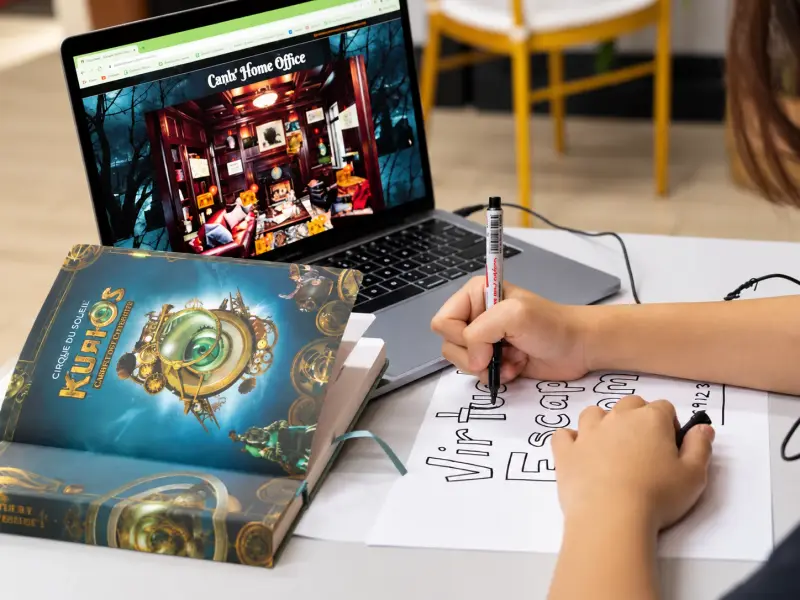 A virtual escape room on a laptop, with a player writing notes beside it