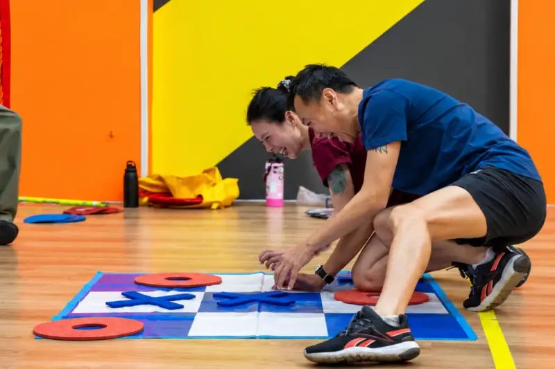 Two players crouch over the giant noughts-and-crosses mat to place a piece