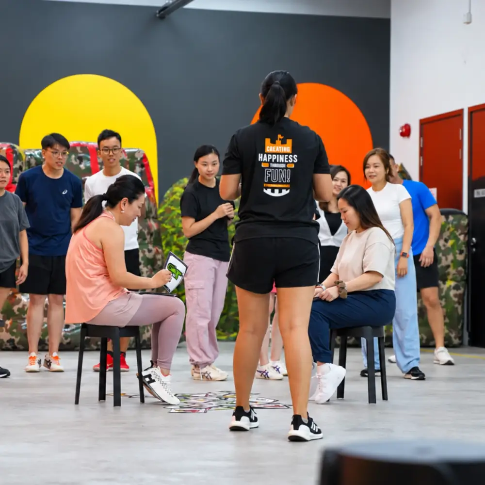 A FunEmpire facilitator runs a round for two seated players while their teams watch
