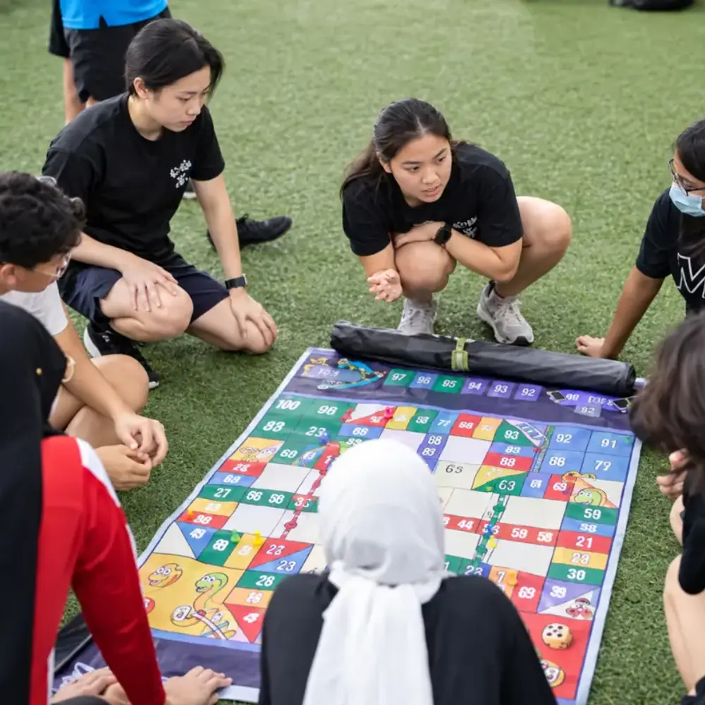 Youth Corps Singapore volunteers gathered around a life-sized Snakes & Ladders mat
