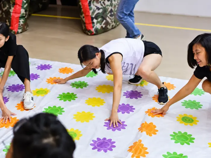 Three players stretch across a life-sized Twister mat