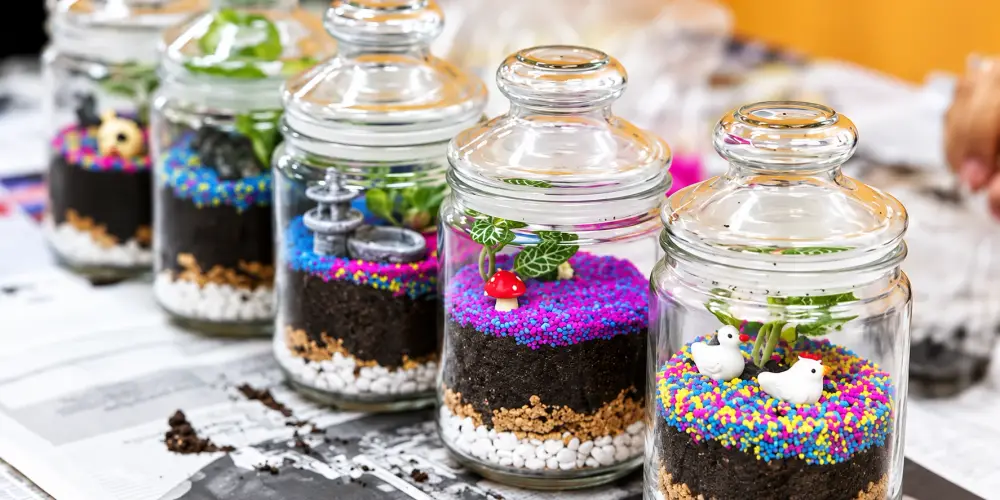 Finished terrariums in lidded glass jars, layered with pebbles, soil and coloured sand