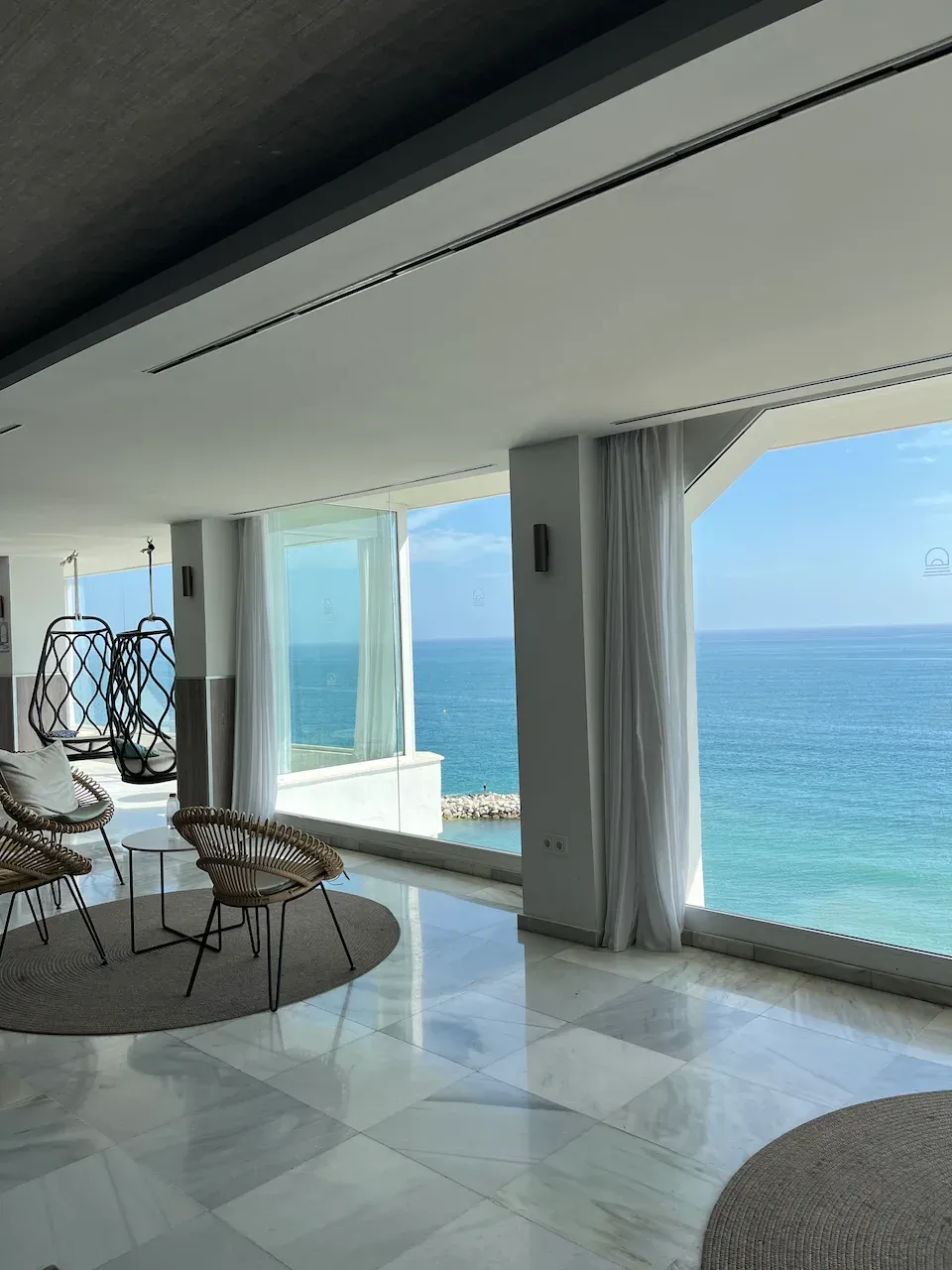 Modern hotel lounge with wicker furniture and hanging egg chairs overlooking the Mediterranean Sea.